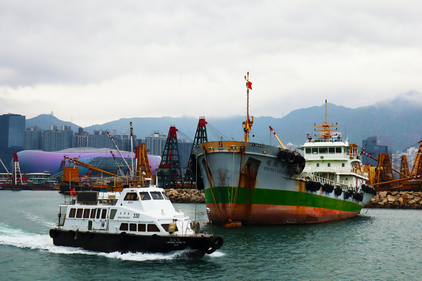 A patrol boat passes a large cargo ship in the harbor.