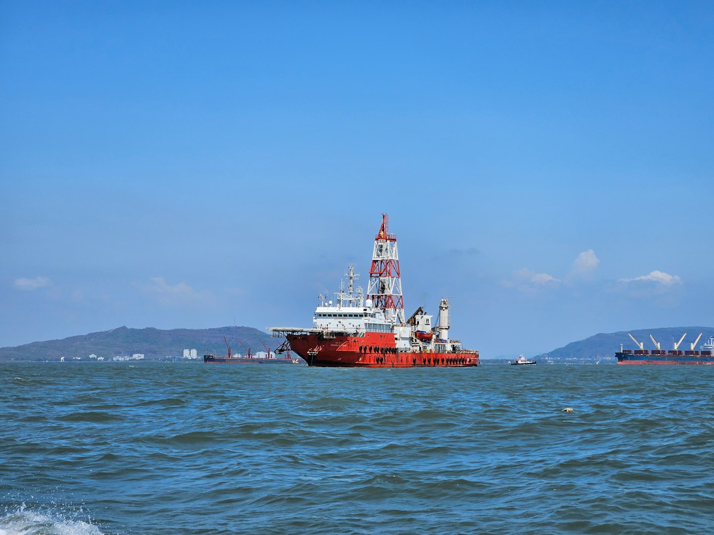 An offshore support vessel navigates choppy waters near coastal mountains.